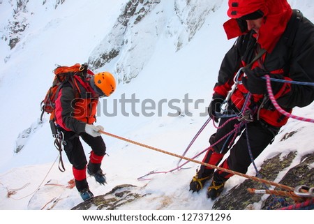 Climber abseiling from the mountain in winter Climber abseiling from the mountain in winter