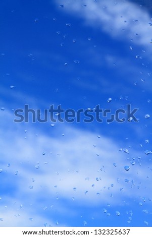 Blue sky and white clouds seen through a rain splashed window