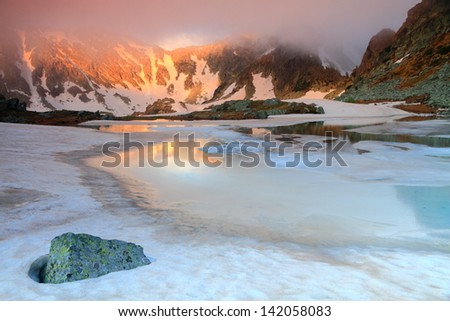 Glacier lake with ice and snow melting in foggy weather on the mountain