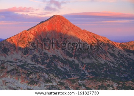 Red light of the rising sun touches the mountain top in the morning
