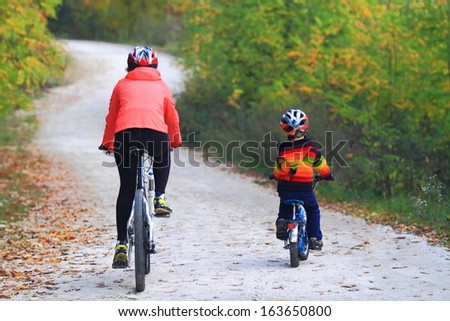 Boy followed by his mother during bike ride in autumn forest