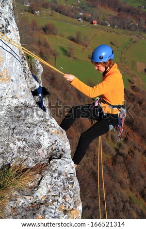 Abseiling woman on vertical rock, high above ground