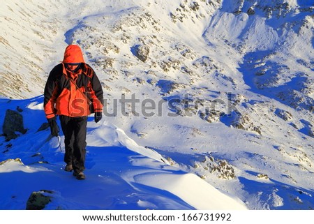 Mountaineer walking a snowy ridge with deep valley behind him