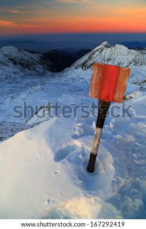 Mountain summit and trail sign covered by snow after sunset