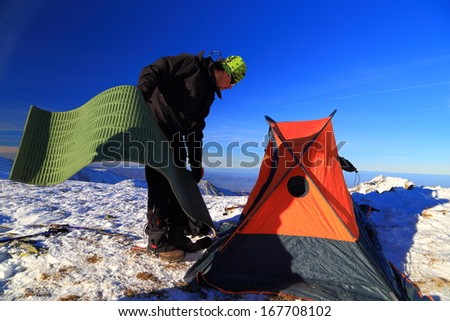 Mountaineer prepares the tent and camping gear on snow field
