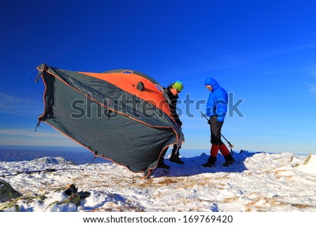 Mountaineers preparing camp and pitching an orange tent in winter