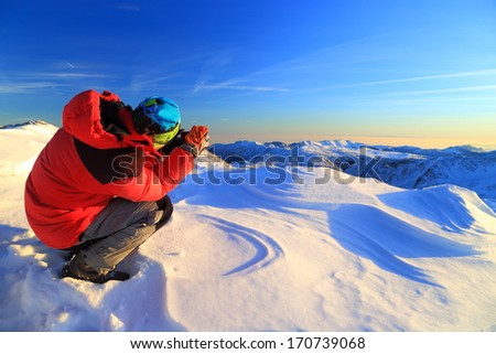 Snowy mountains being photographed by hiker at sunset