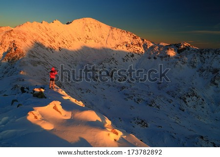 Snowy mountains under the sunset light and standing hiker admires the view
