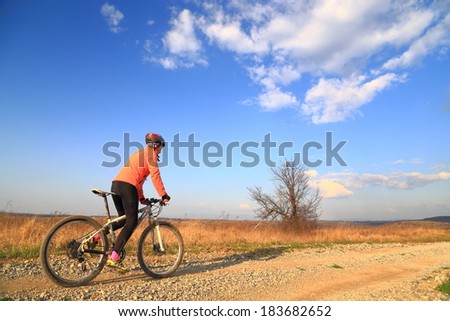 Woman cyclist riding on a dirt road in sunny afternoon