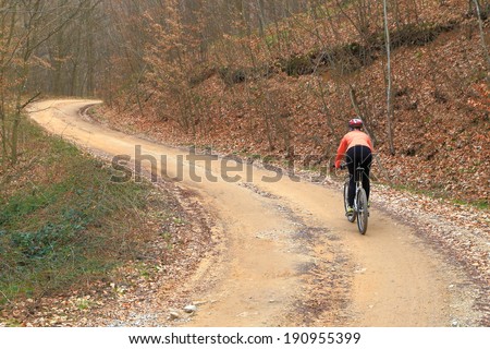 Young woman biking on winding forest road in autumn