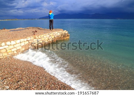 Woman on small pier watching the Mediterranean sea before the storm begins, Greece