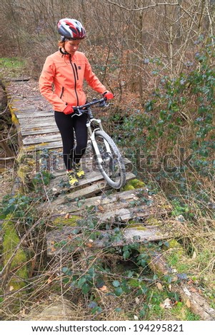 Woman carries a mountain bike across old wooden bridge