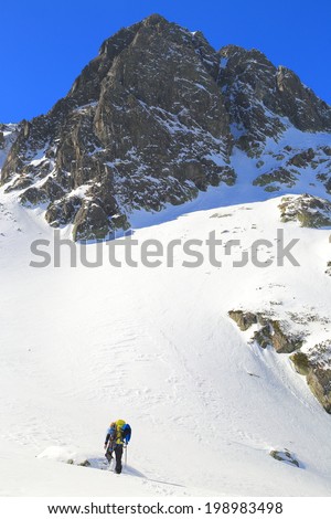 Remote mountaineer ascending steep snowy summit