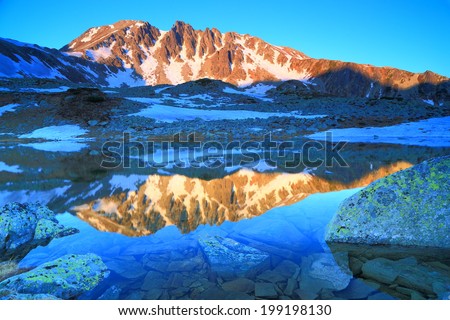 Blue mountain lake reflecting steep summits in the morning