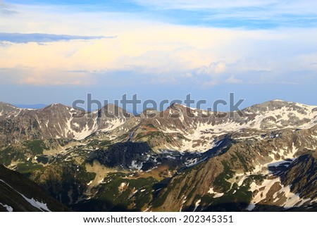 Mountain summits spotted with snow under blue sky and white clouds at sunset