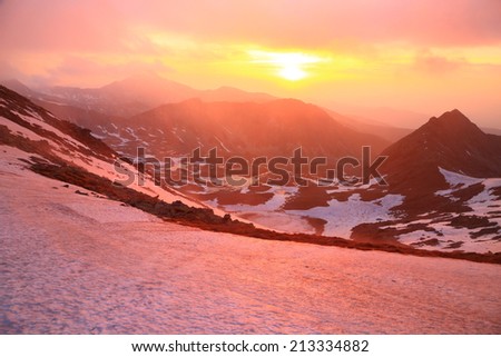 Snow covered valley and red sun at sunset above mountains