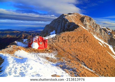 Long clouds above mountain ridge and red emergency shelter in sunny autumn morning