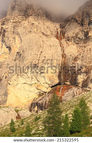 Tall waterfall pouring from upper plateau of Sella massif, Dolomite Alps, Italy