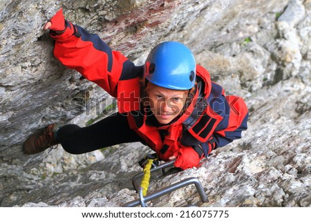 Woman climbs on narrow gap between rock walls on via ferrata \