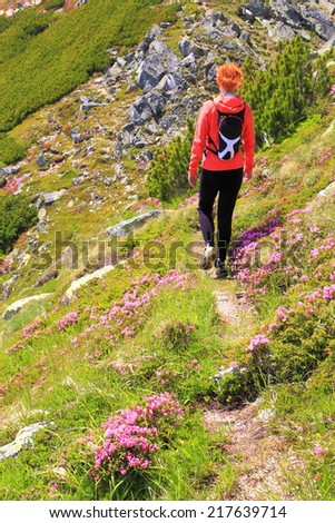 Young woman walks a narrow trail surrounded by pink mountain flowers