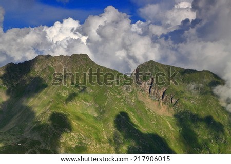 Green mountain slopes shadowed by large white clouds in summer