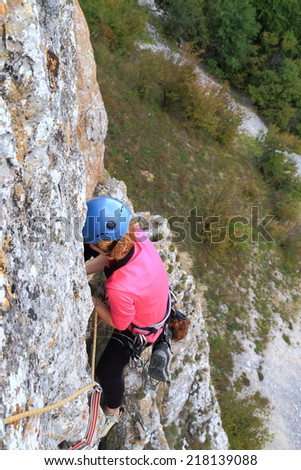 Woman climbs high above ground on a steep rock wall