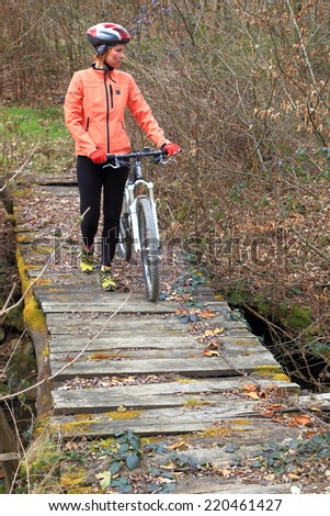 Autumn day with young woman with a bike walking across old wooden bridge