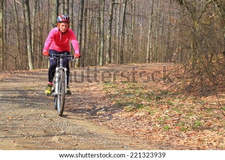 Sunny autumn day in the forest with woman cycling on a dirt road
