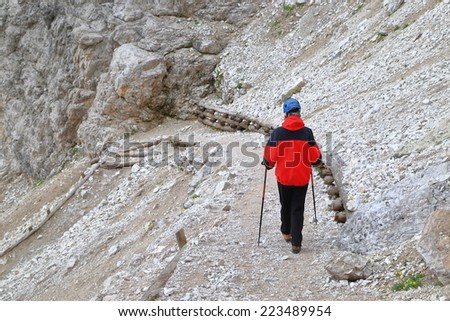 Woman climber walking a rocky trail beneath Pomedes refuge, Dolomite Alps, Italy