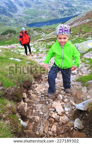 Happy kid climbs a winding mountain trail followed by his mother