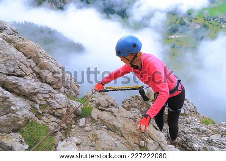 Climber woman clips the safety gear on via ferrata 