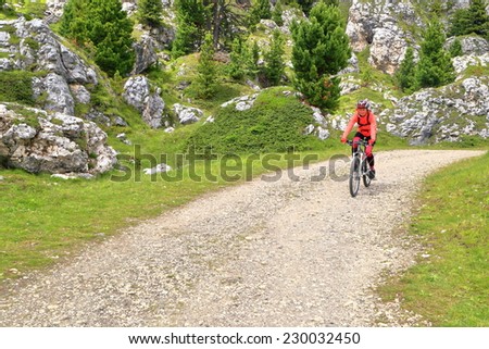 Young woman pedaling on wide trail near Sella pass, Dolomites Alps, Italy