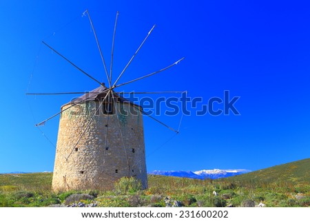 Spring day on the Greek hills with sunlit building of traditional wind mill and distant snowy mountains, Greece