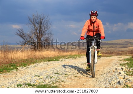 Dark sky behind young woman cycling on a dirt road in sunny day