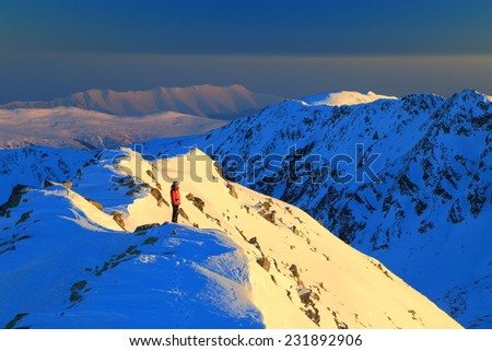 Distant mountaineer admiring the setting sun on a snowy mountain