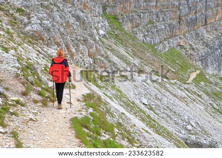 Woman hiker follows a trail near along tall walls of Dolomite Alps, Italy