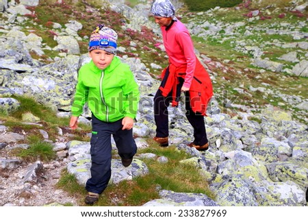 Young boy happy to climb the mountain trail followed by his mother