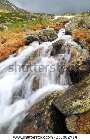 Fast water jumps over rocks on a mountain in autumn day