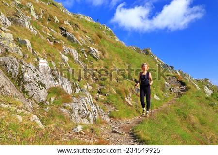Distant woman walking on narrow trail on the side of the mountain in sunny day