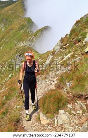 Narrow mountain trail with woman hiking near the clouds