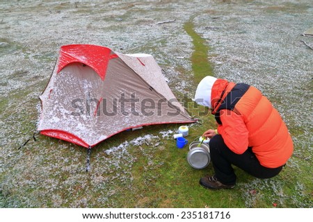Small tent and hiker preparing food in cold weather