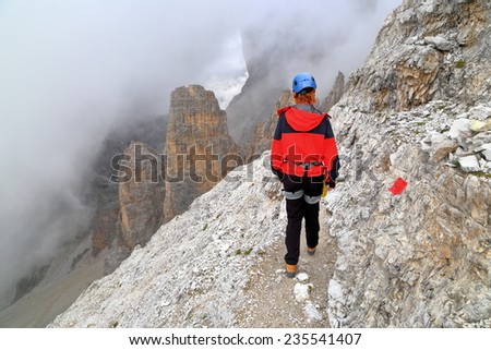 Clouds above the mountains and woman climber walking on aerial  trail, via ferrata \