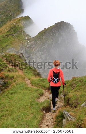 Alpine trail and woman hiker walking above the clouds
