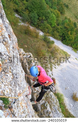 Climber woman hanging on climbing gear above distant ground beneath her
