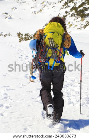 Mountaineer carries a backpack and climbing gear on snow covered trail