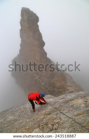 Rock spire embedded in fog and woman climbing via ferrata 