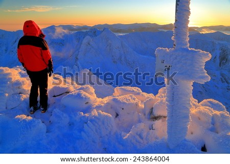 Snow covered ,ountain summit with hiker standing and watching the sunset