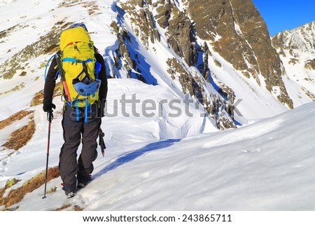 Mountaineer with climbing gear and yellow backpack on snow covered mountain