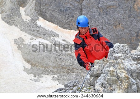 Climber woman clips the safety gear to steel cable of via ferrata \