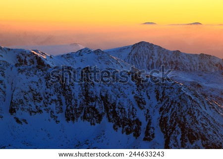 Darkness cover tall snowy mountains under orange sky after sunset